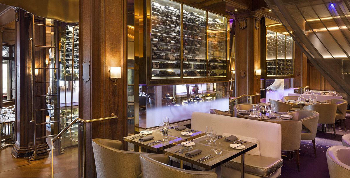 A luxe restaurant interior with a wall of wine bottles behind glass.