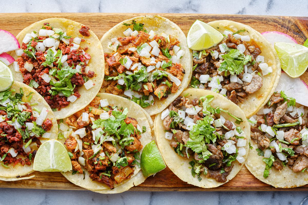 A wooden board full of open tacos with fillings.