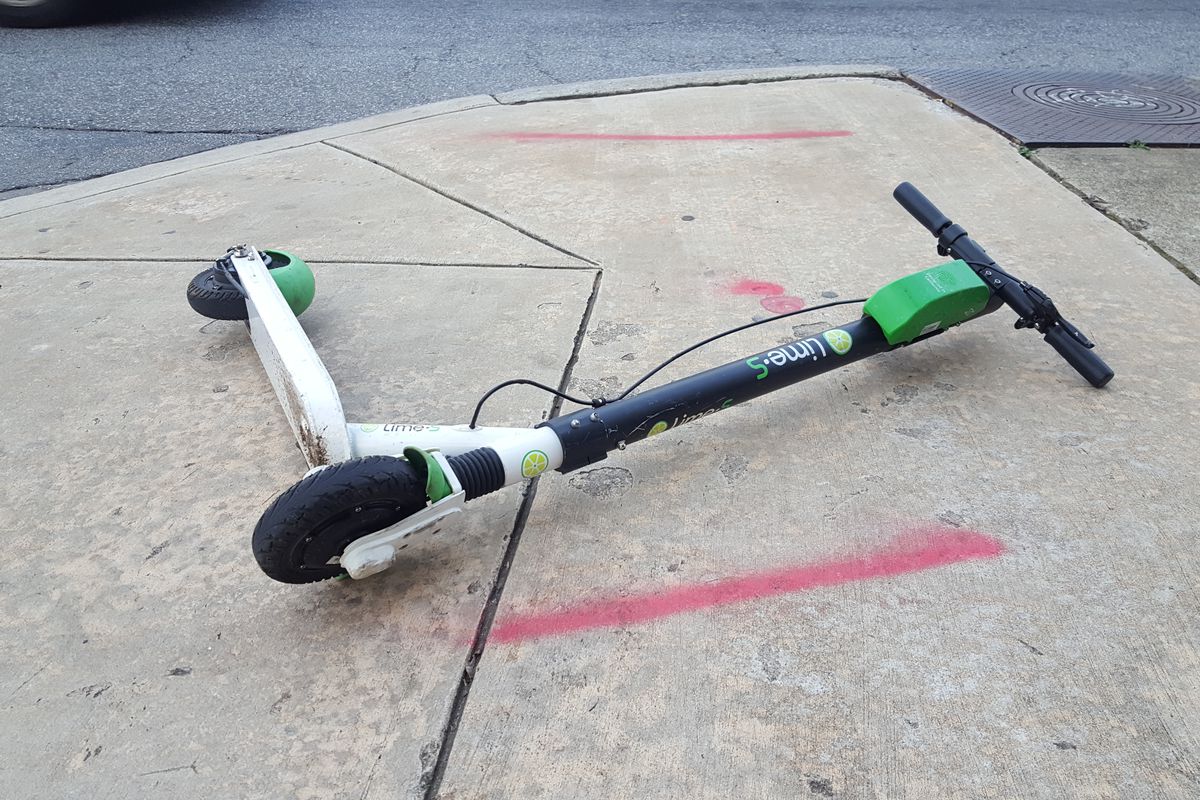 A bright green e-scooter sits tipped over on a sidewalk.