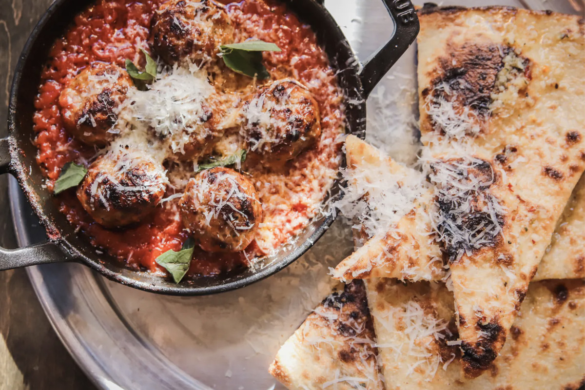 A cast-iron pot holds meatballs and tomato sauce beside grilled triangles of flatbread.