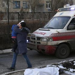 A woman carrying a child walks past the body of a child covered with a cloth after shelling between Russian-backed separatists and Ukrainian government forces in a residential area of the town of Artemivsk, Ukraine, Friday, Feb. 13, 2015. Despite a looming cease-fire deal for eastern Ukraine, a government-held town 40 kilometers (25 miles) behind the front line has been hit by shelling, killing at least one person. The deadline for the warring sides to halt hostilities is Sunday morning at one minute after midnight. 