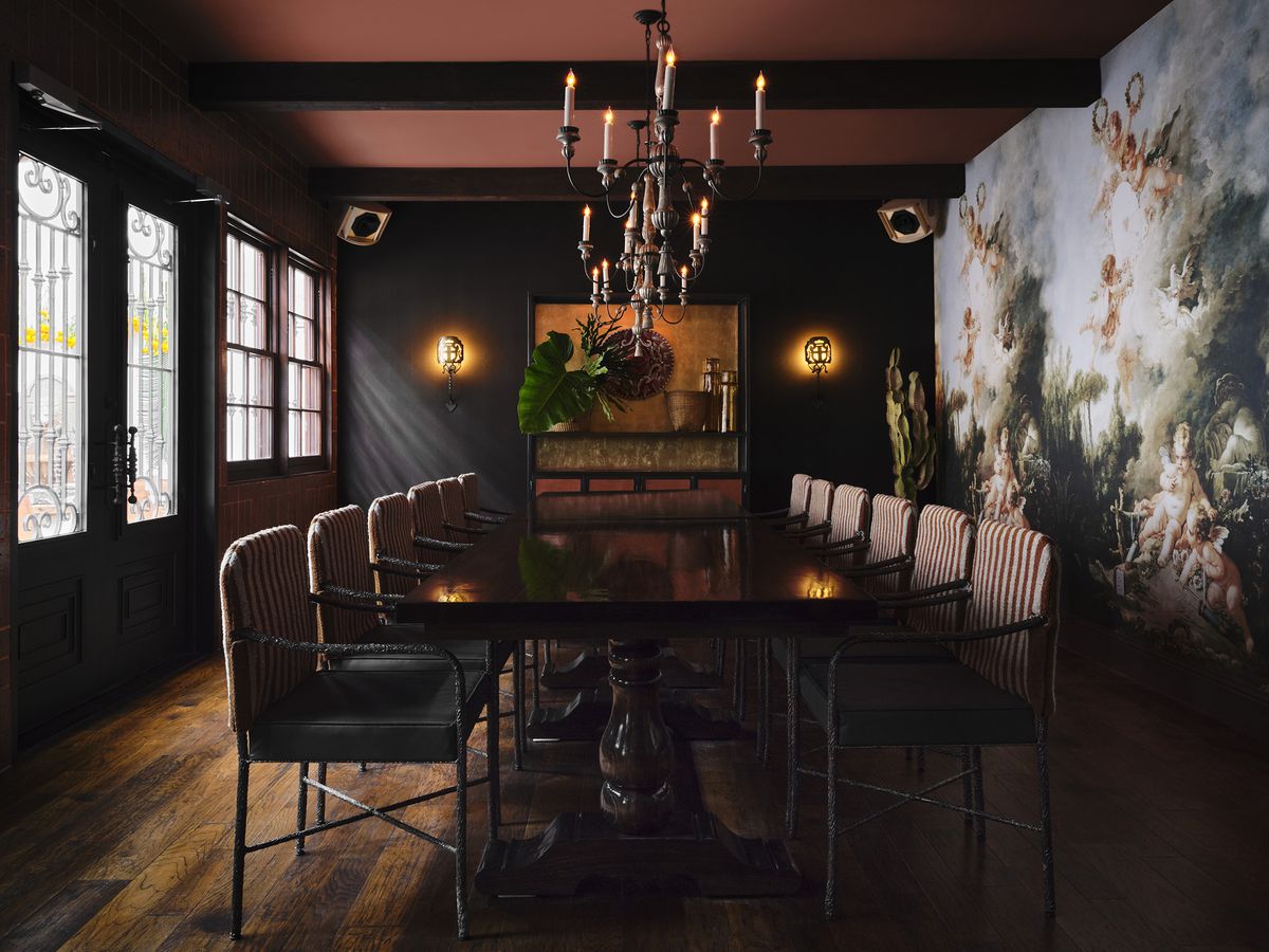 A private dining room features wooden floors, a black accent wall, a fresco of angles, a brownish red ceiling, and a table for 10.