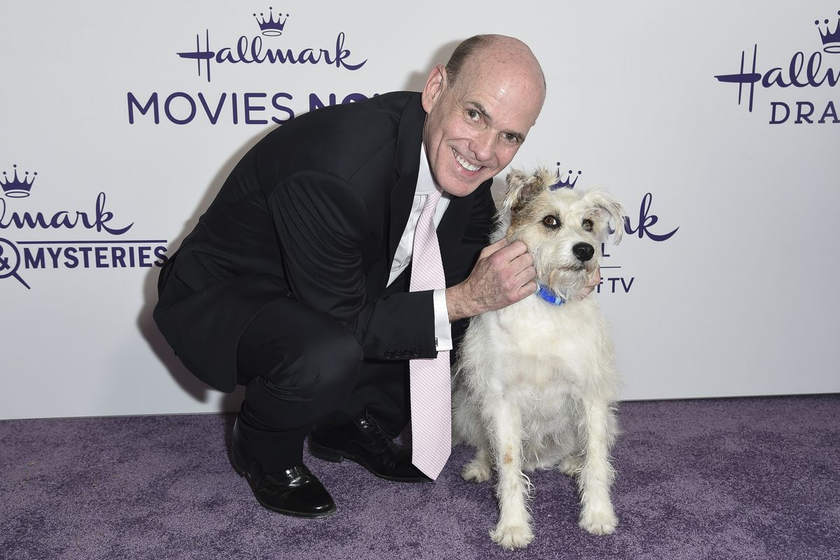 FILE - This July 26, 2018 file photo shows Bill Abbott, left, with a dog named Happy at Hallmark’s Evening Gala during the TCA Summer Press Tour in Beverly Hills, Calif. The head of Hallmark’s media business is leaving the company after 11 years. No reason was given for Bill Abbott’s departure as CEO of Crown Media Family Networks, and no replacement was immediately named. (Photo by Richard Shotwell/Invision/AP, File)