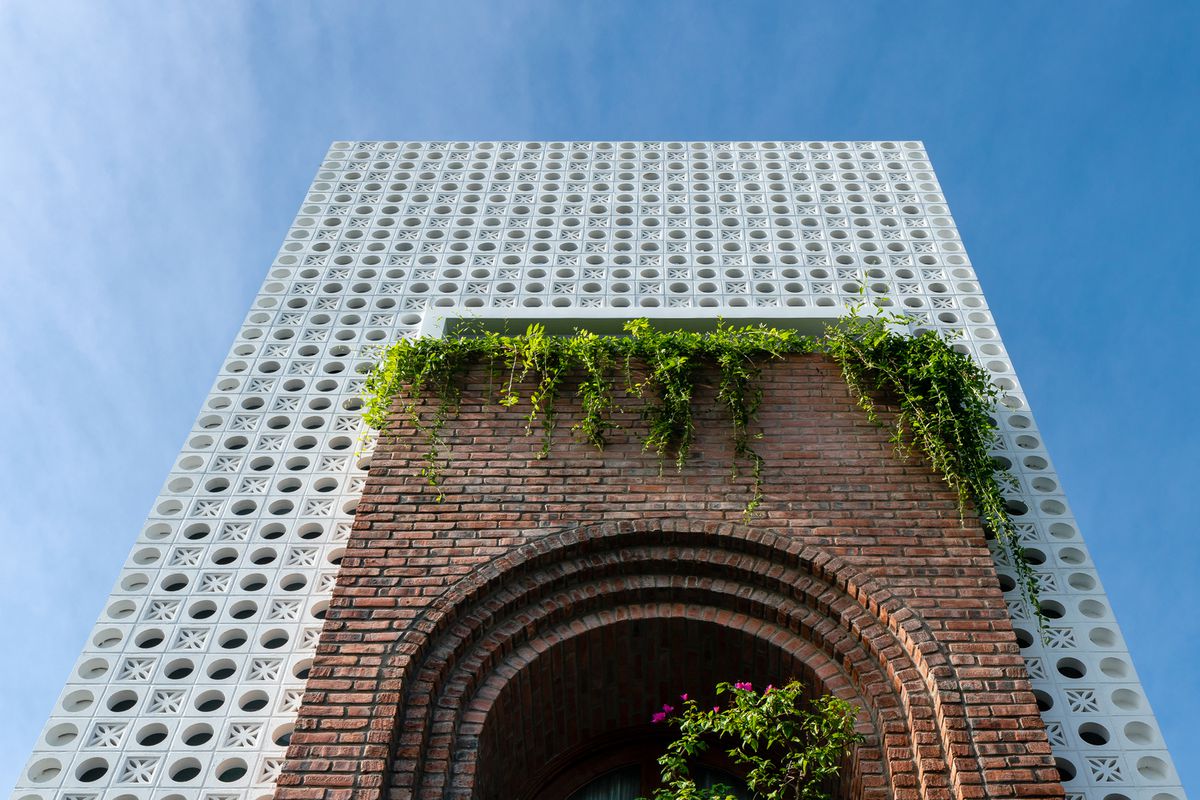 A three-story building boasts a white perforated facade and a brick arch for the entrance. 