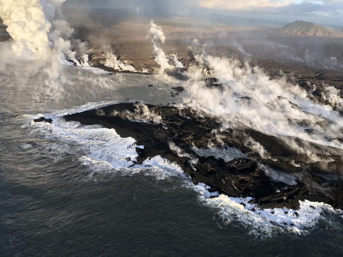 The coast of Hawaii seen from above, with steam clouds where lava is meeting the sea.