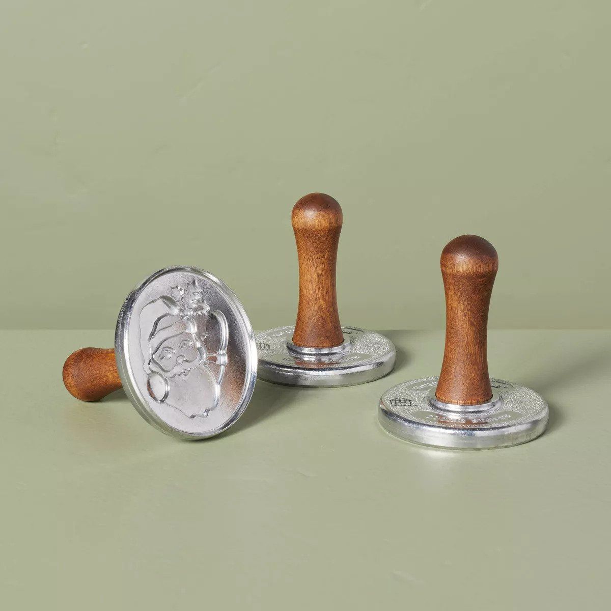 A set of three cookie stamps with wood handles. One is on its side to display a Santa engraving.