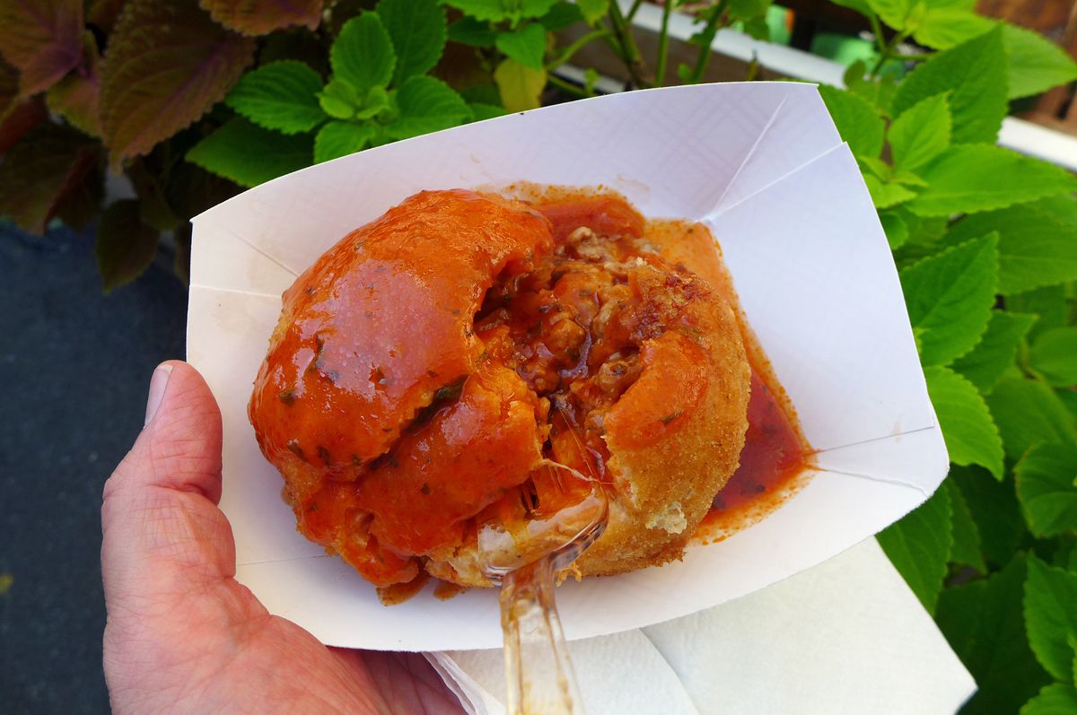 A rice ball in a paper boat covered in tomato sauce.