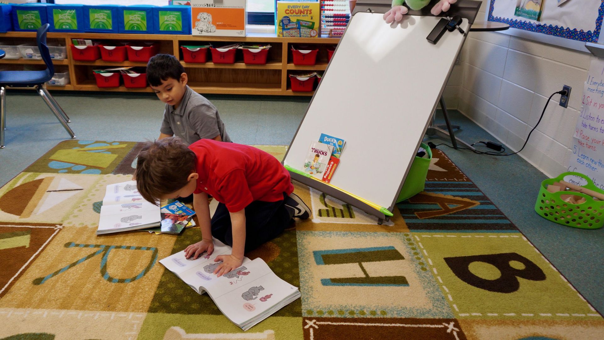 Two children read picture books in a classroom.