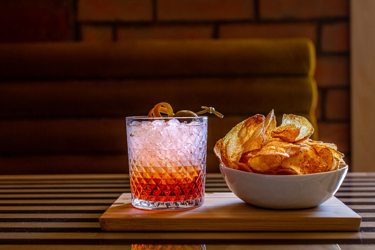 a cocktail in a short glass with a bowl of potato chips.