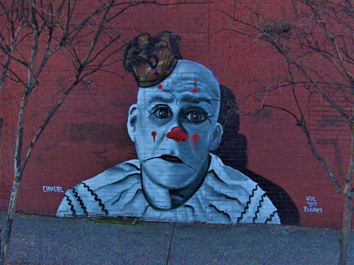 A mural of a sad clown painted on a red brick wall.