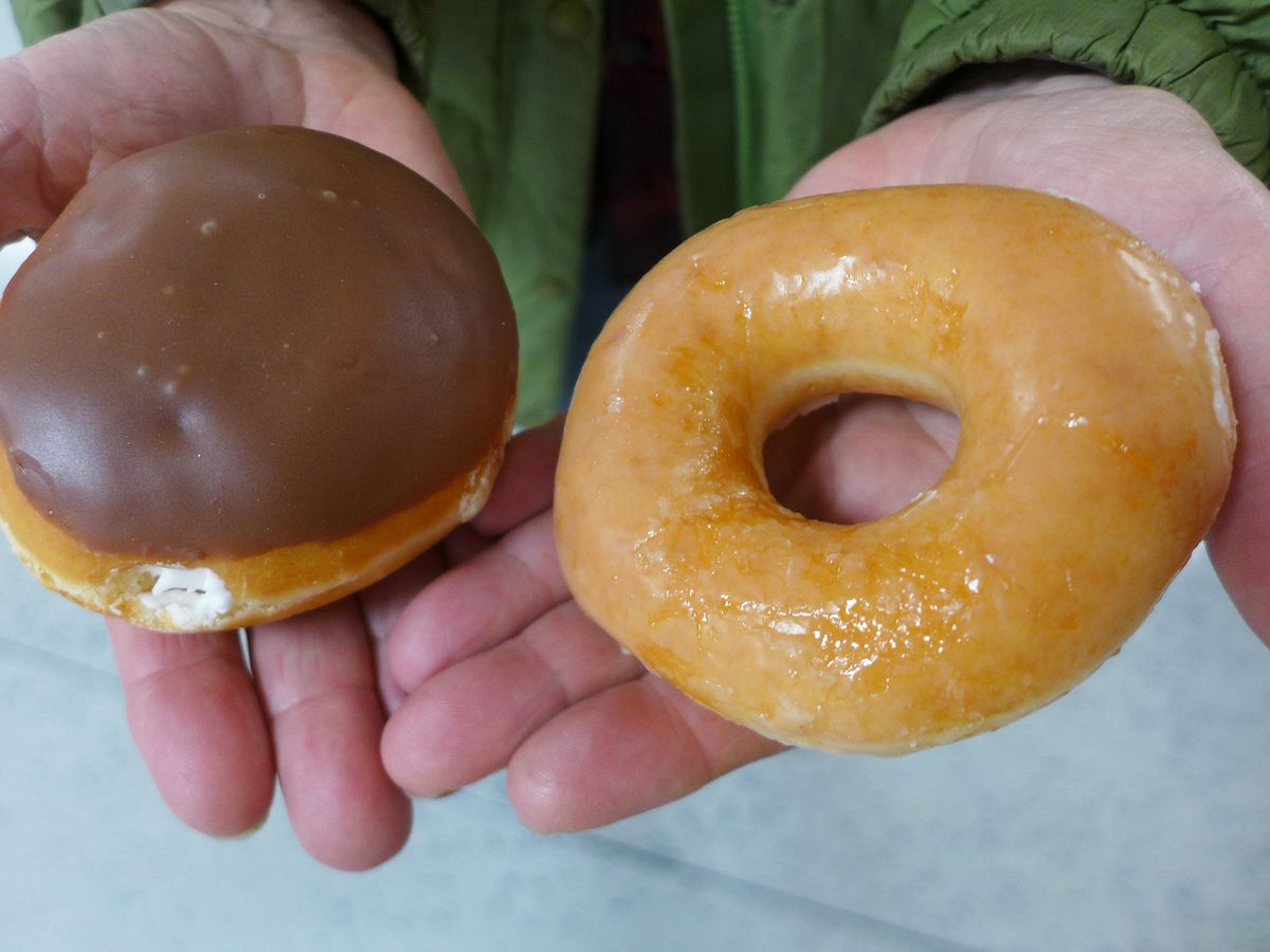 Two doughnuts held on the palms of two intersecting hands, one with chocolate frosting, one simply glazed.