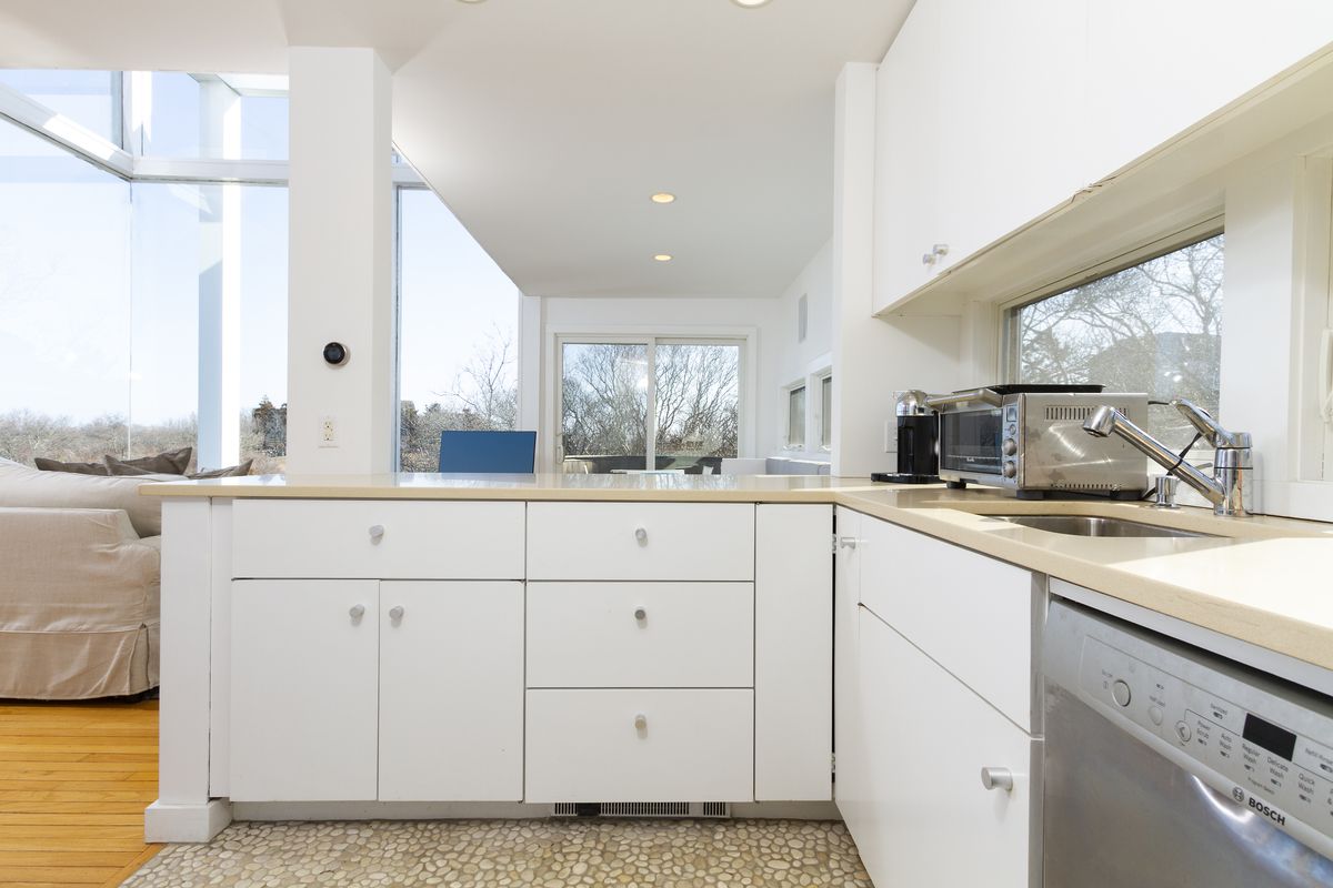 A kitchen has white cabinets, beige countertops, and an open view onto the living room. 