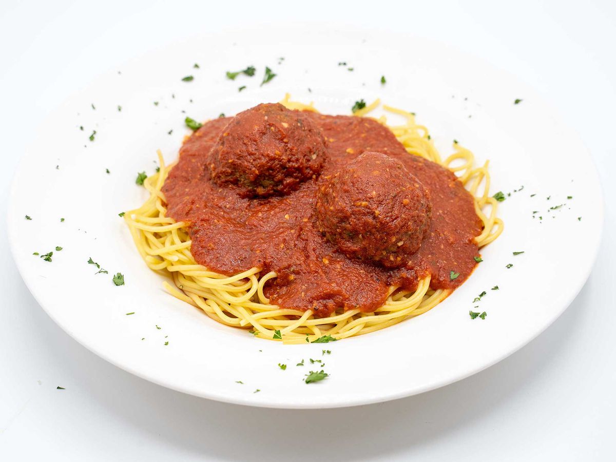 A white plate of spaghetti and meatballs on a white background. 