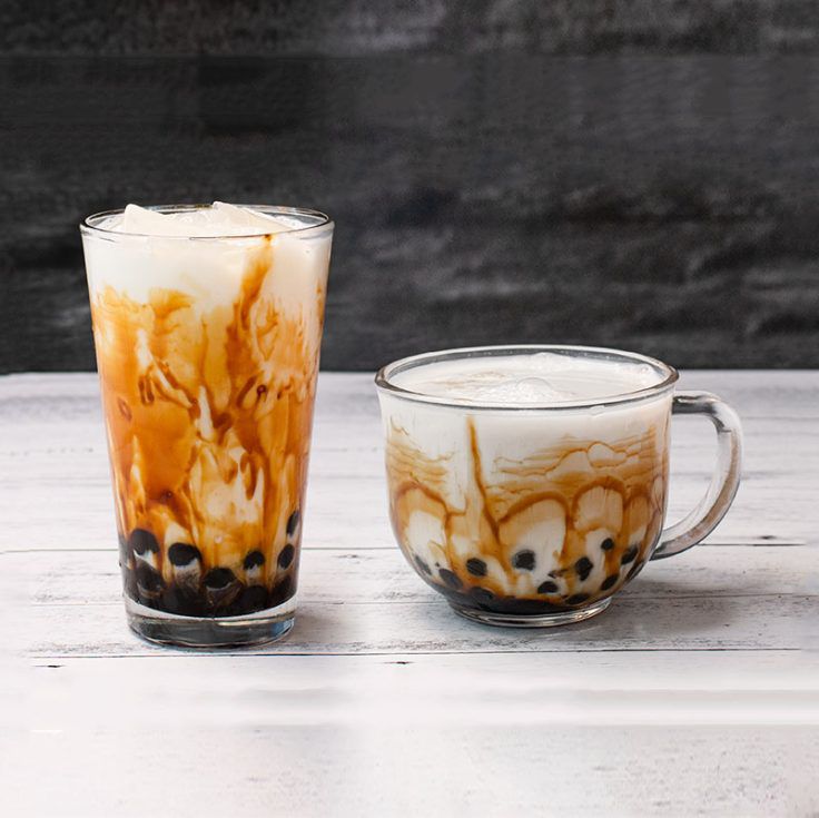 A tall clear glass with a liquid that is white and brownish with black balls at the bottom next to a clear mug with the same content. 