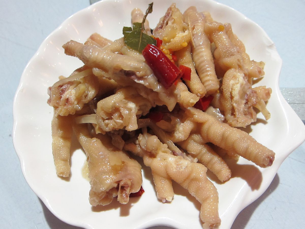 A pile of pale chicken feet dotted with red peppers on a shell-shaped plate.