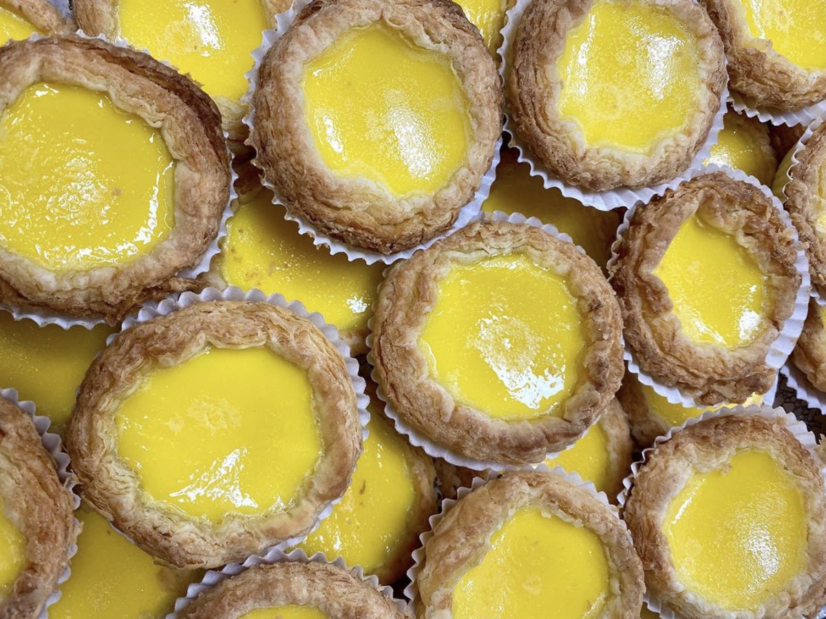 A stack of golden-yellow egg tarts in aluminum tins