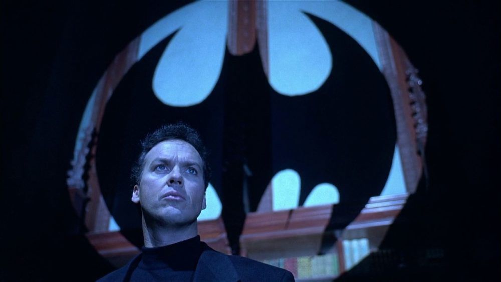 Bruce Wayne (Michael Keaton) standing in front of a silhouette of the bat signal in Batman Returns.