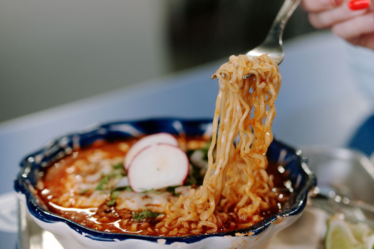 A fork pulls noodles out of a bowl of birria ramen.