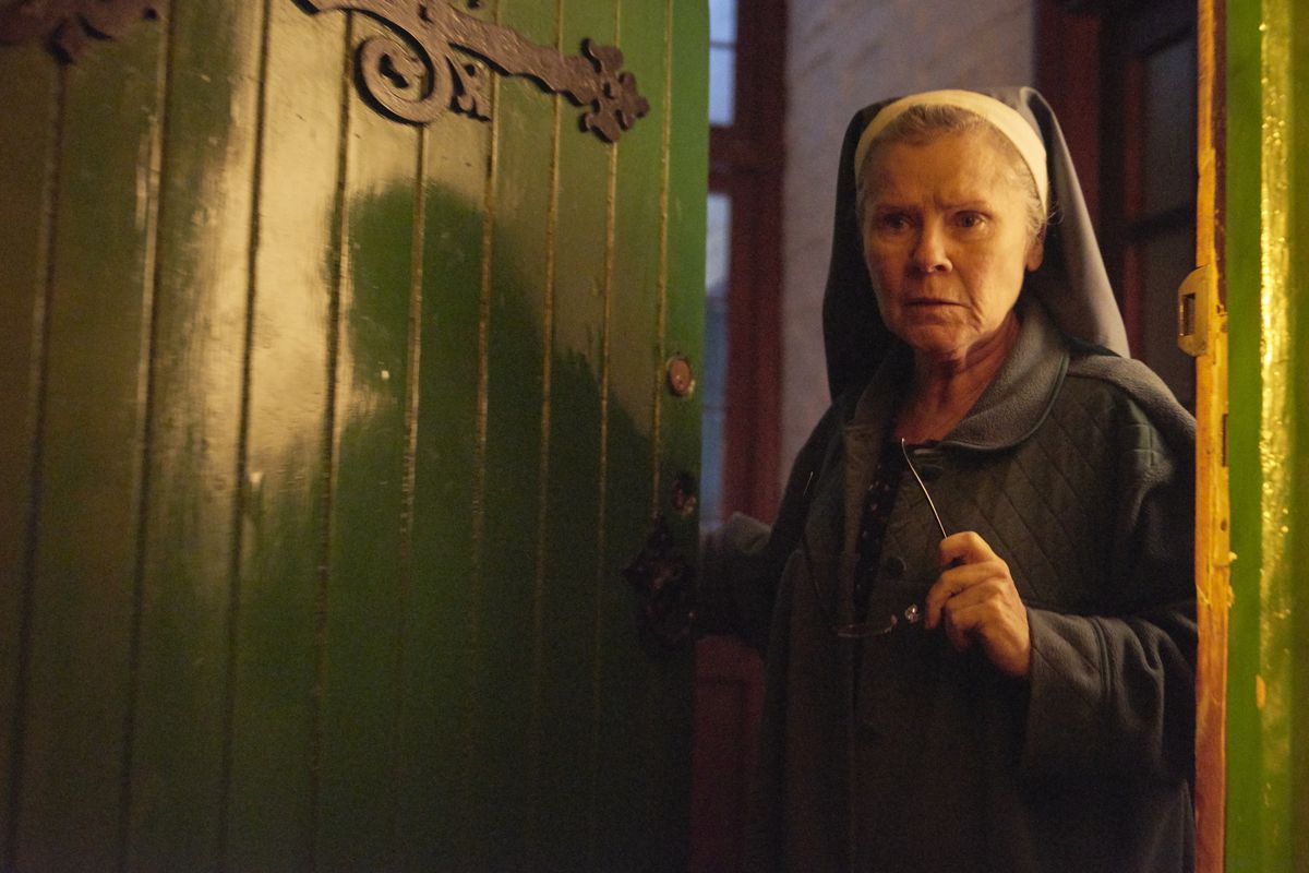 Imelda Staunton, playing a nun, stands in front of a bright green door in Romola Garai’s horror movie Amulet.
