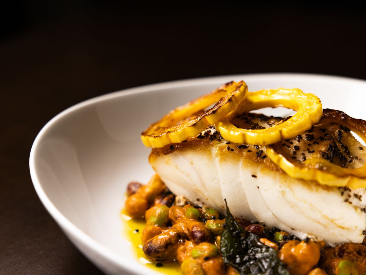 Chilean sea bass cooked Chennai-style with bean ragu, delicata squash, curry leaf, mustard oil, and ninja radish in a white bowl at Kahani restaurant.