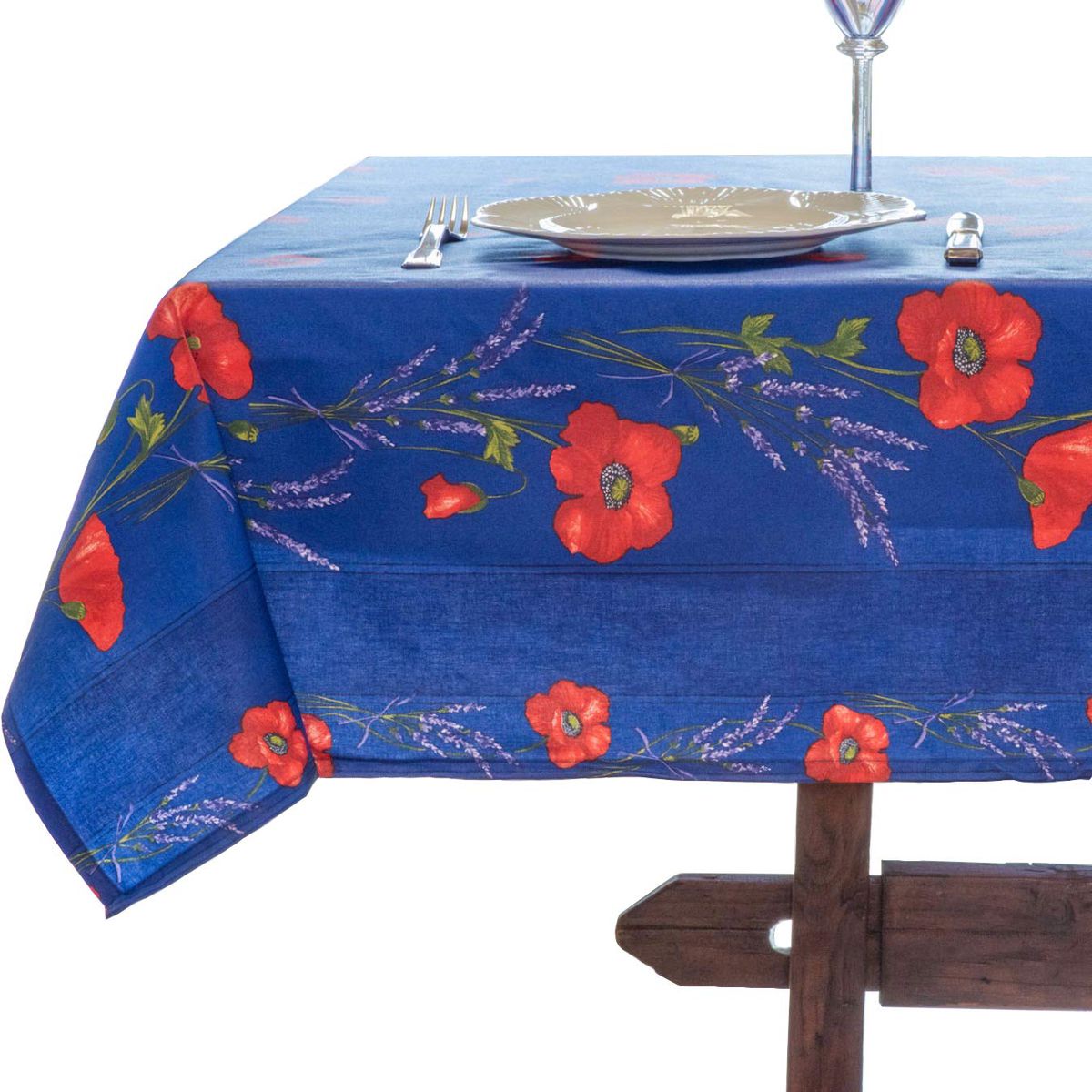A blue tablecloth features French Provencal poppies on it. There is a white plate and silverware on the table.  