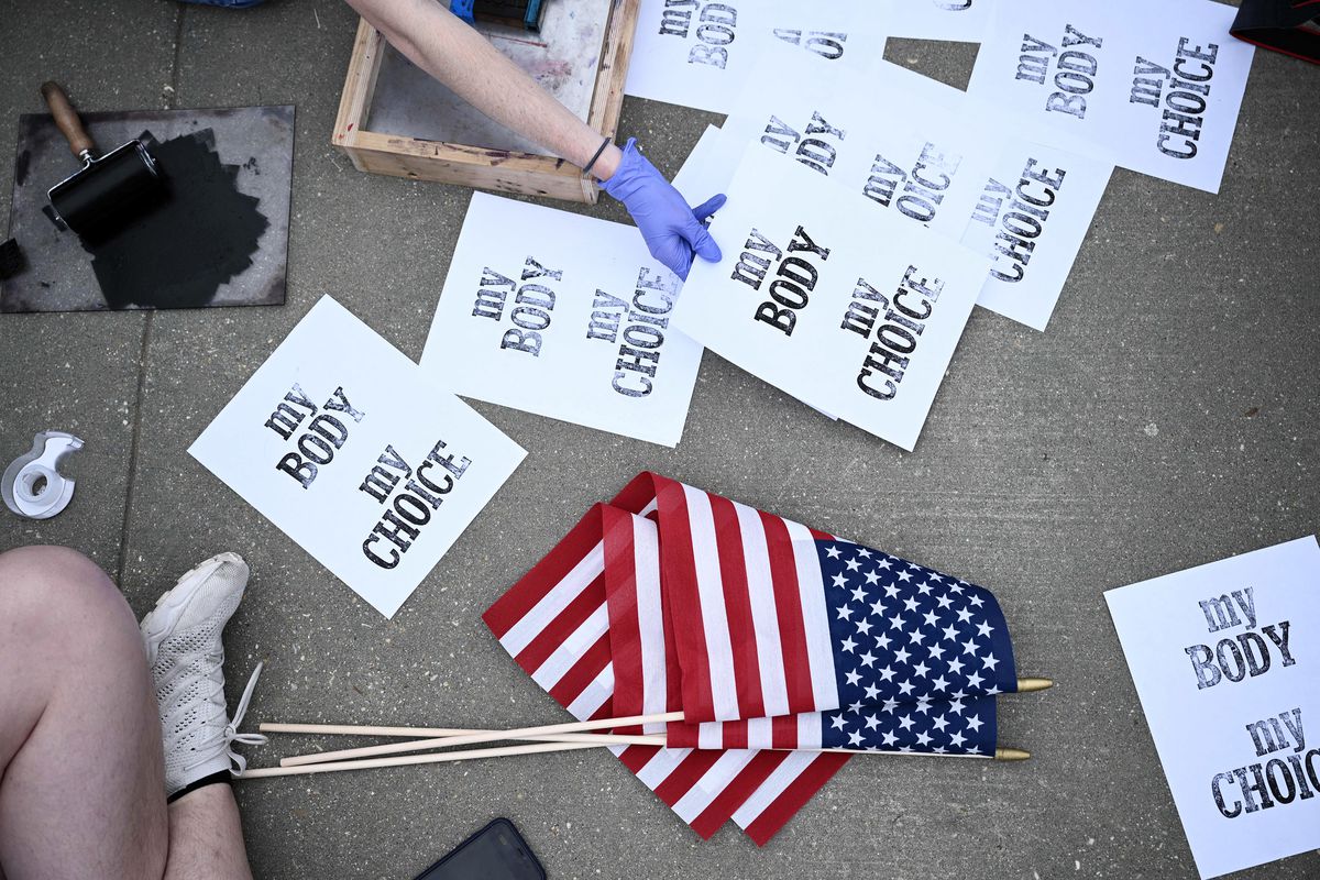 Aerial shot of signs on the ground that read “My body, my choice” beside a pile of American flags on sticks.