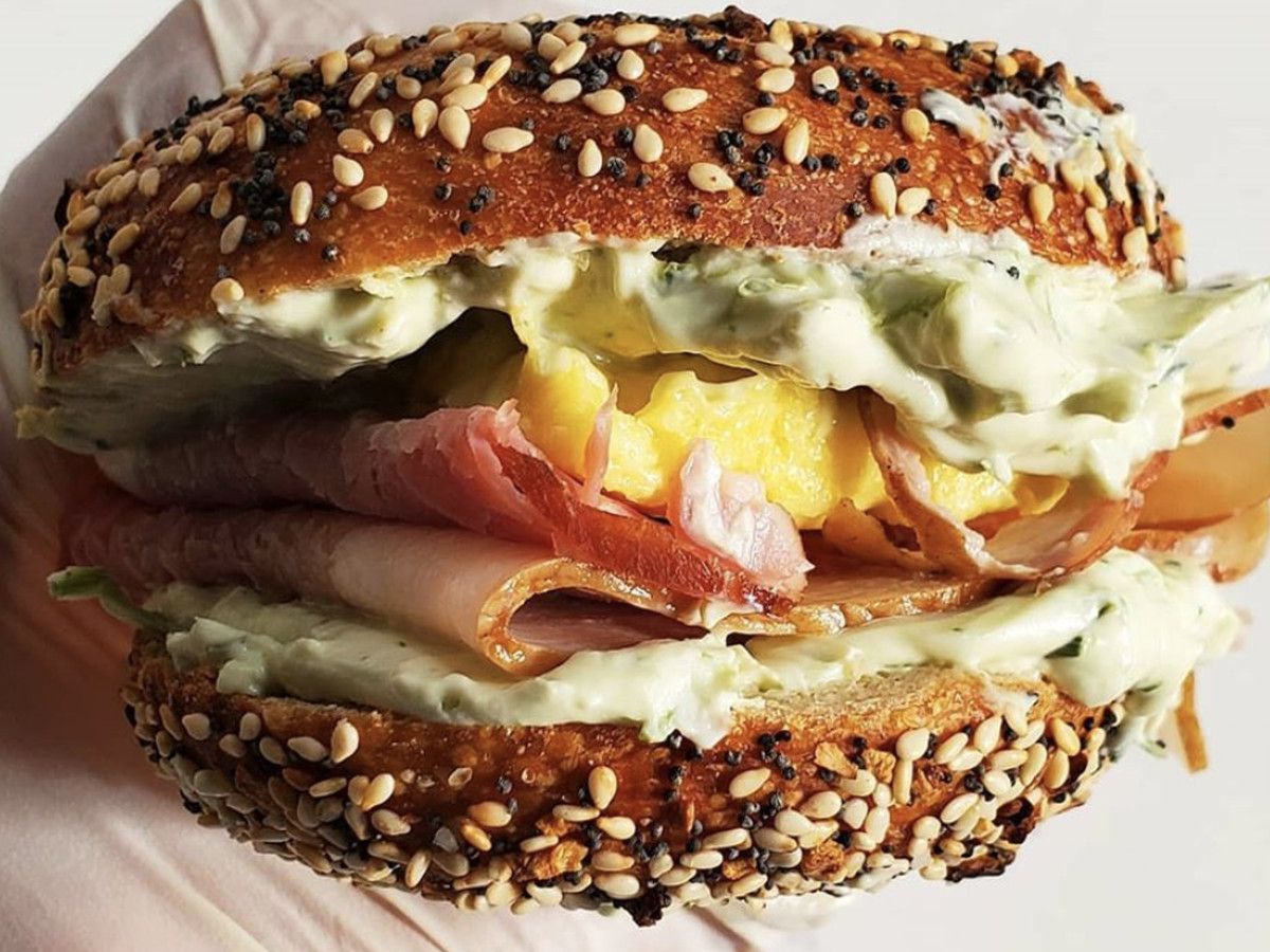 Sideview of scrambled eggs, ham, and tarragon cream cheese on a bagel at Porkchop &amp; Co.
