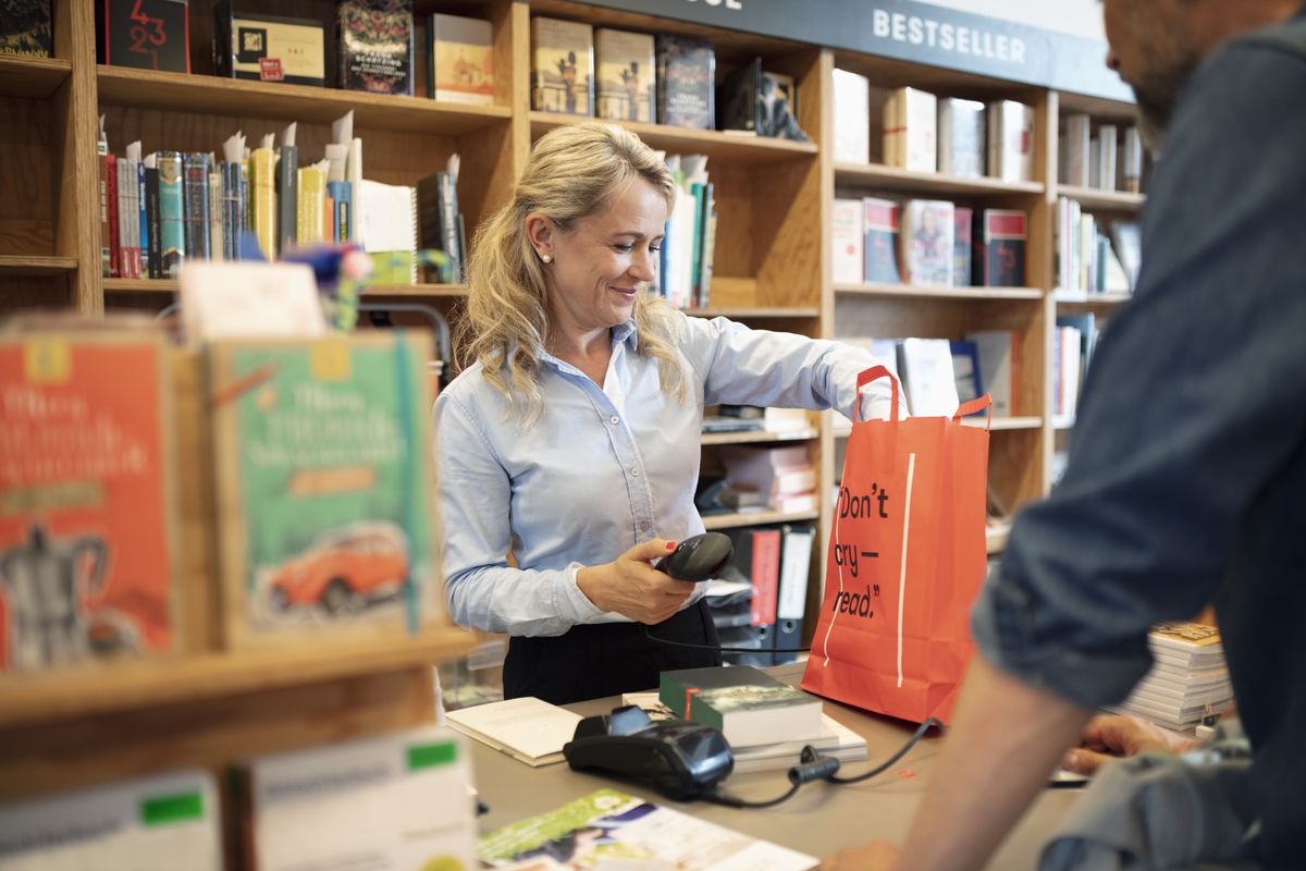 A clerk behind the counter in a bookstore puts a customer’s purchases in a shopping bag.