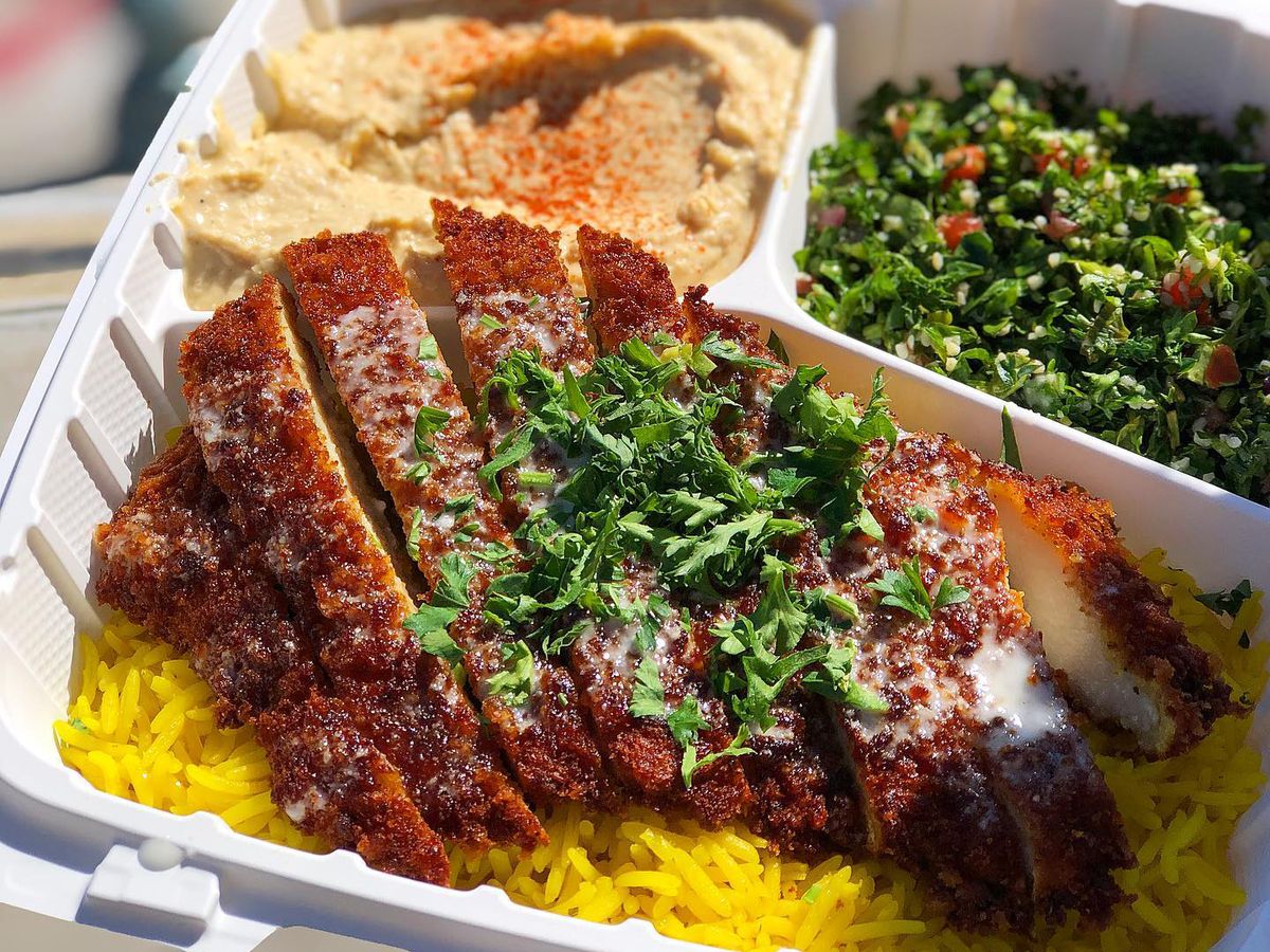 A to-go container with fried chicken on rice, hummus, and tabouli.