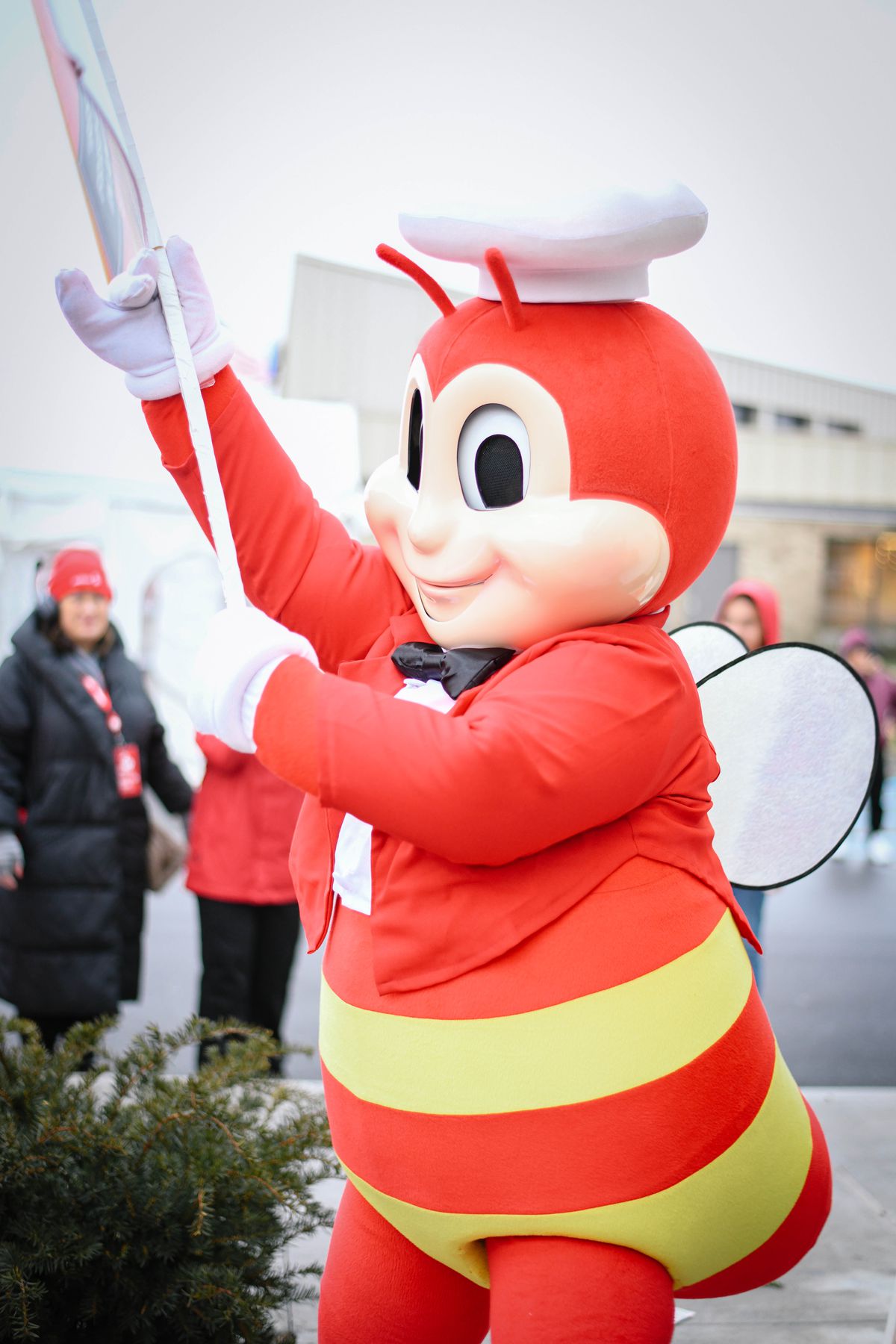 A red and yellow bee with a white chef hat and white wings and a black bow tie holding something.