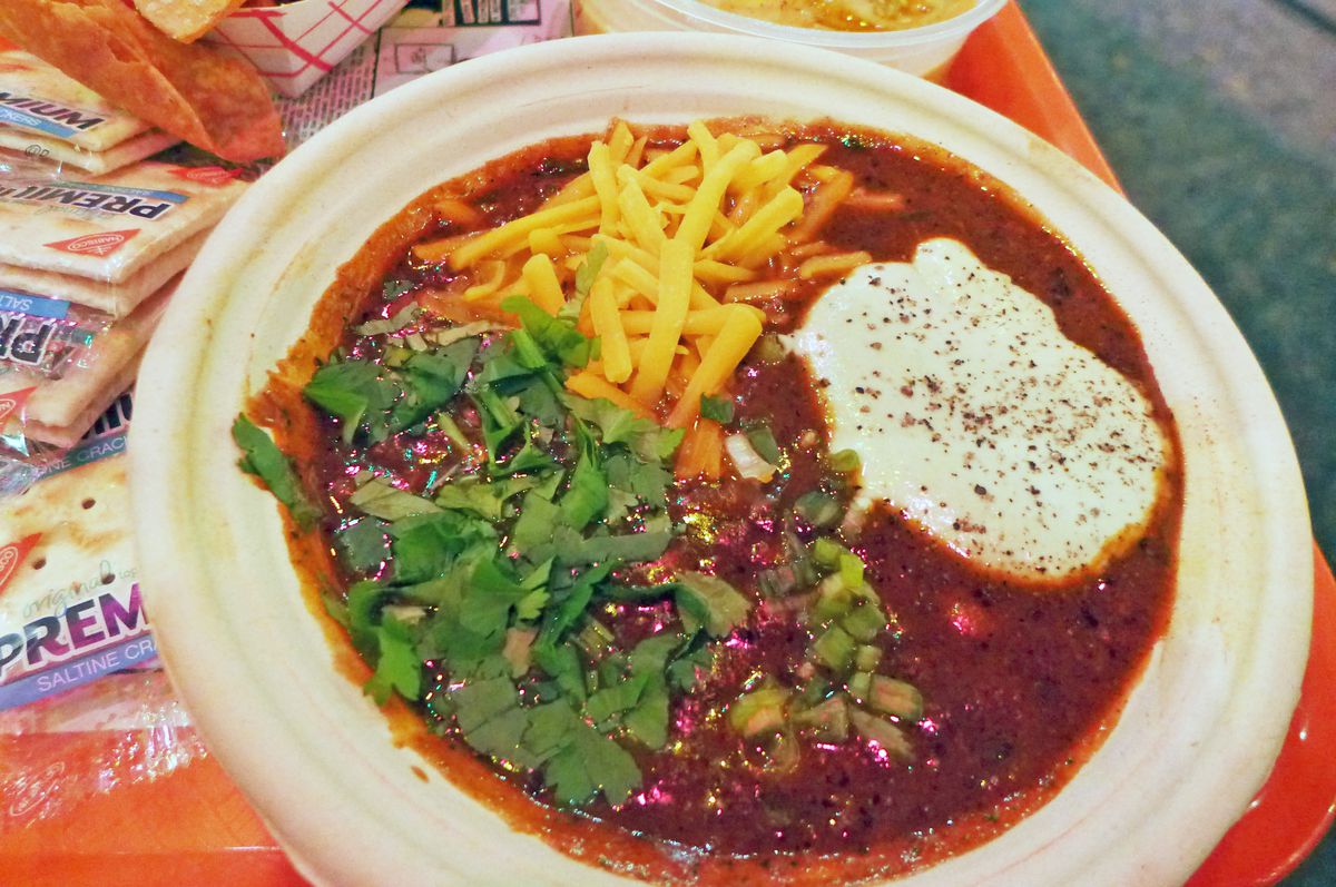A bowl of chili with shredded cheese floating on top and packaged saltines on the side.