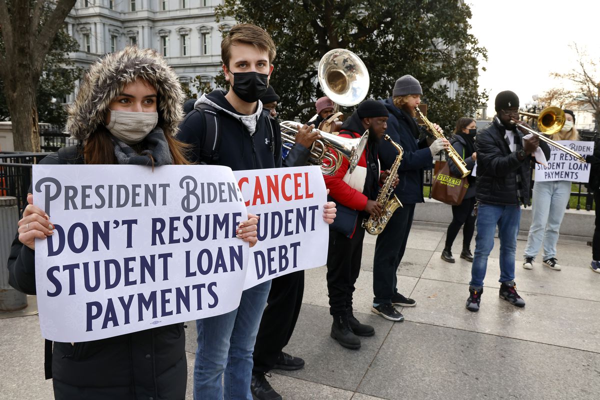 Protesters standing outdoors near the White House hold signs that read, “Cancel student debt,” and, “President Biden, don’t resume student loan payments.”