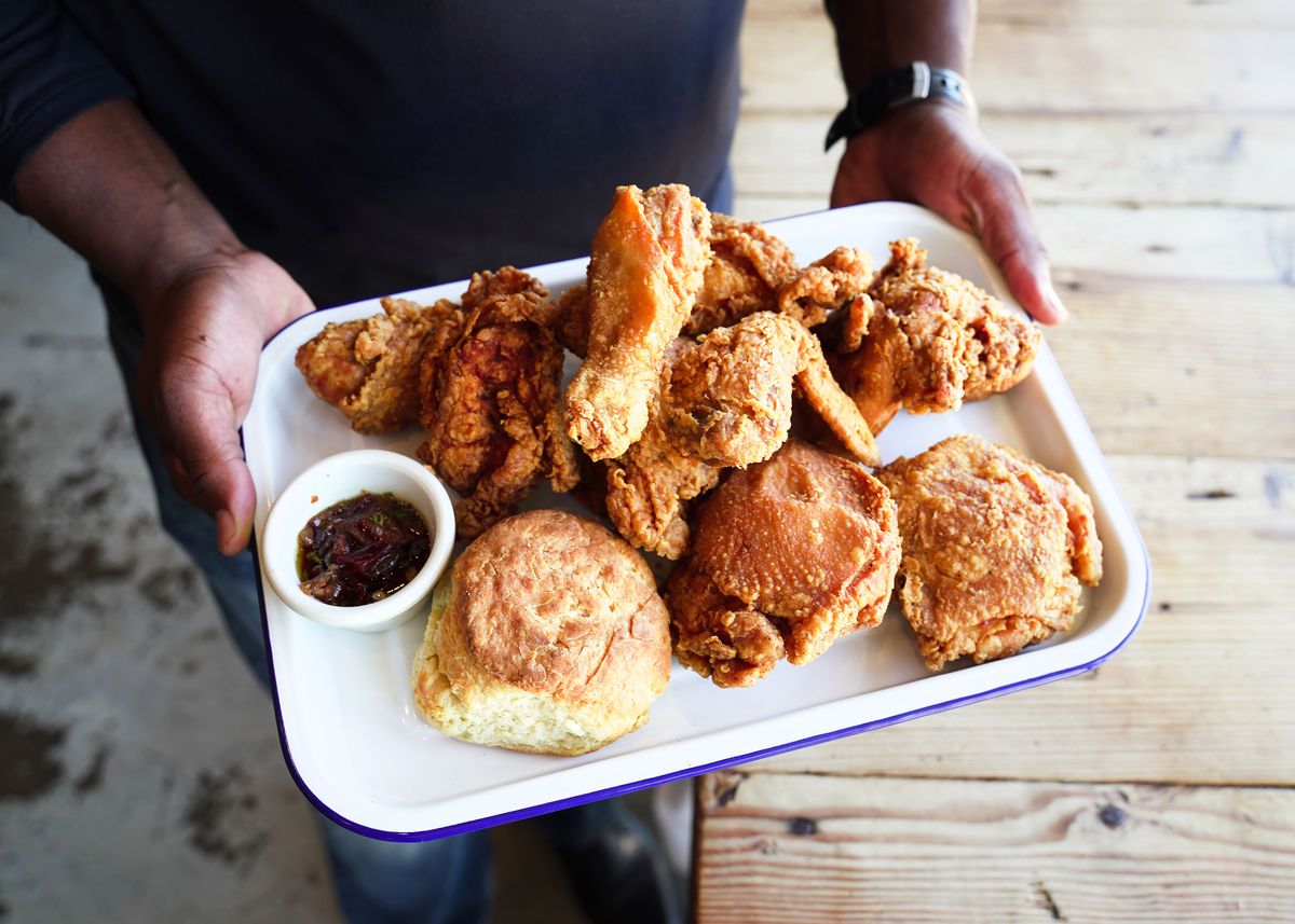Greg Gatlin holding a tray of fried chicken, a biscuit, and a dipping sauce.