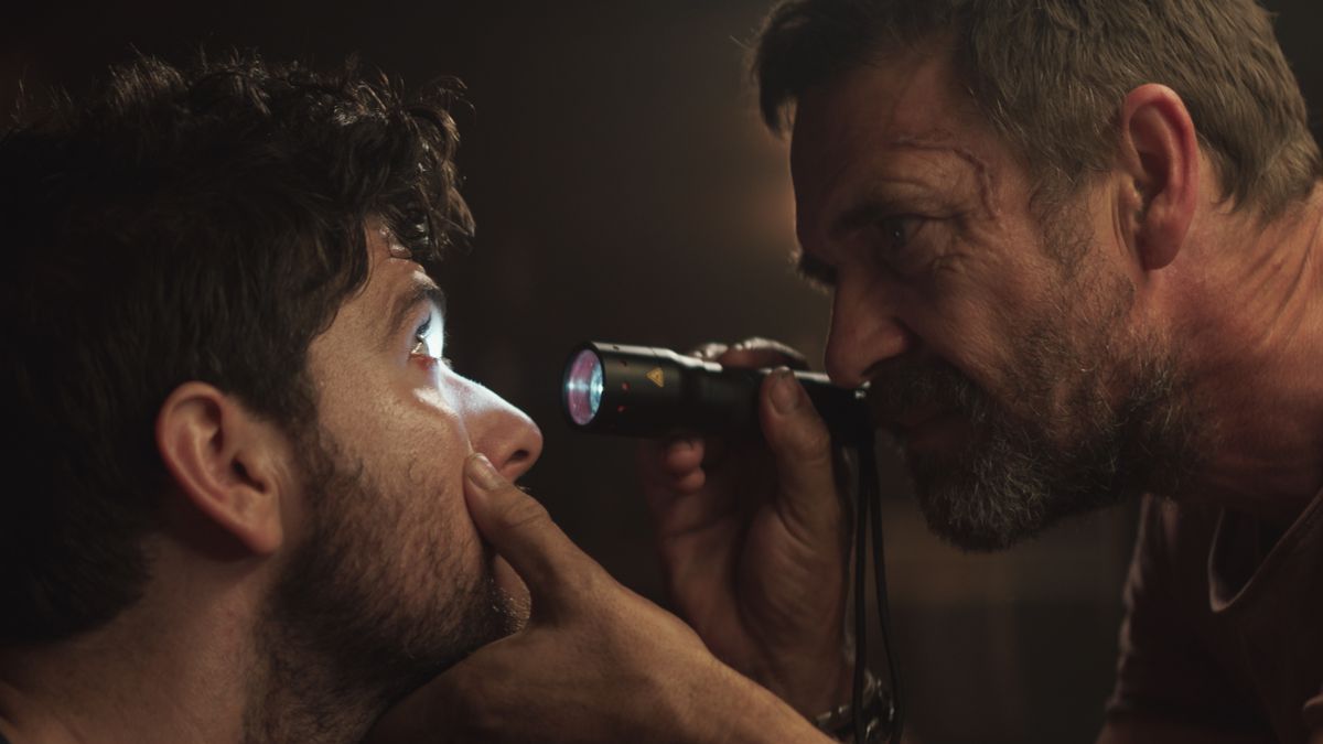 One grim looking-man shines a flashlight into another’s eyes while examining him for parasitic contagion in the horror movie Sea Fever.