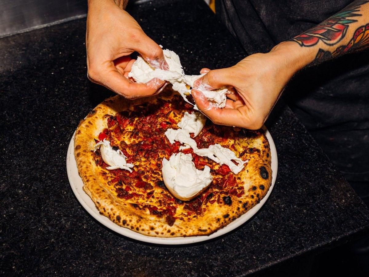 A chef tears cheese to top a pizza.