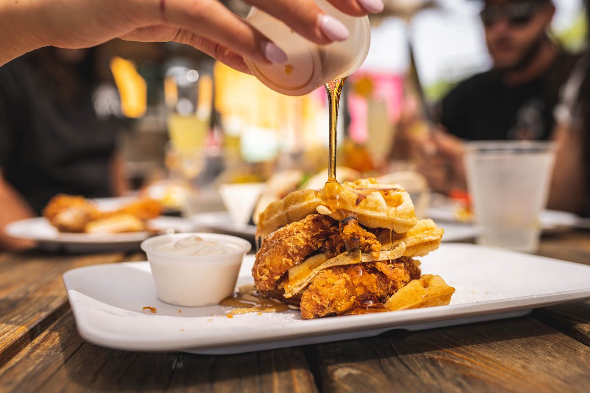 pouring syrup over a layered stack of fried chicken and waffles