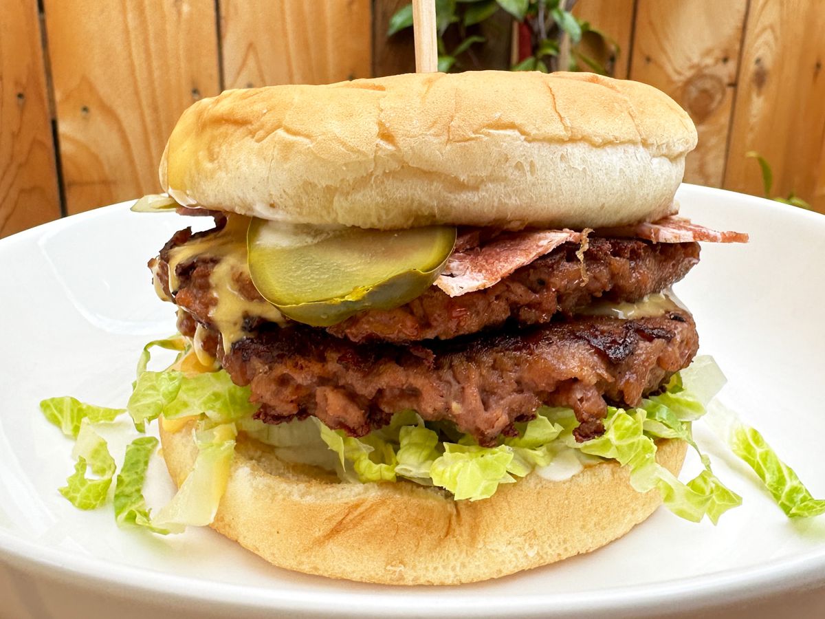 A photo of the Double Bacon Lodge Burger with Beyond patties and vegan bacon at V3 PDX food cart