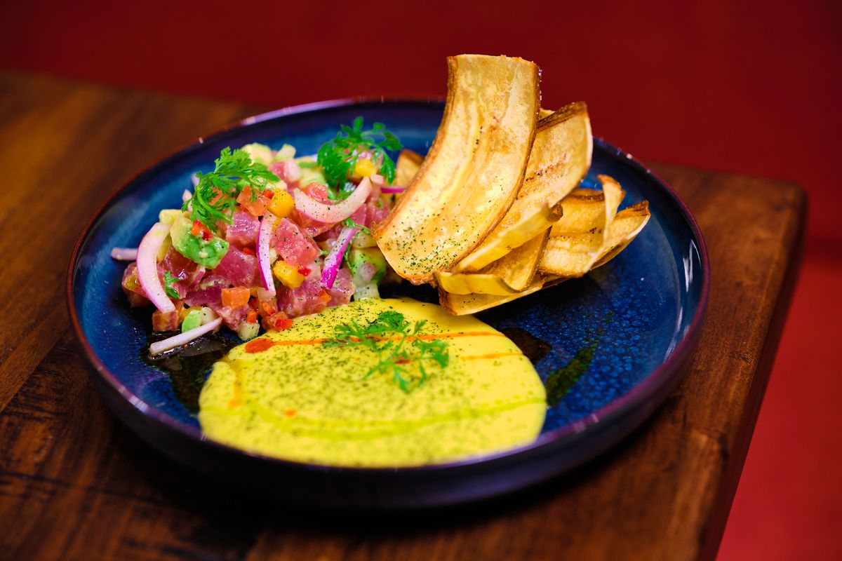 A bright blue ceramic plate is filled with vibrant ceviche and yellow sauce with crispy plantain chips from Atla Toro in Atlanta. 
