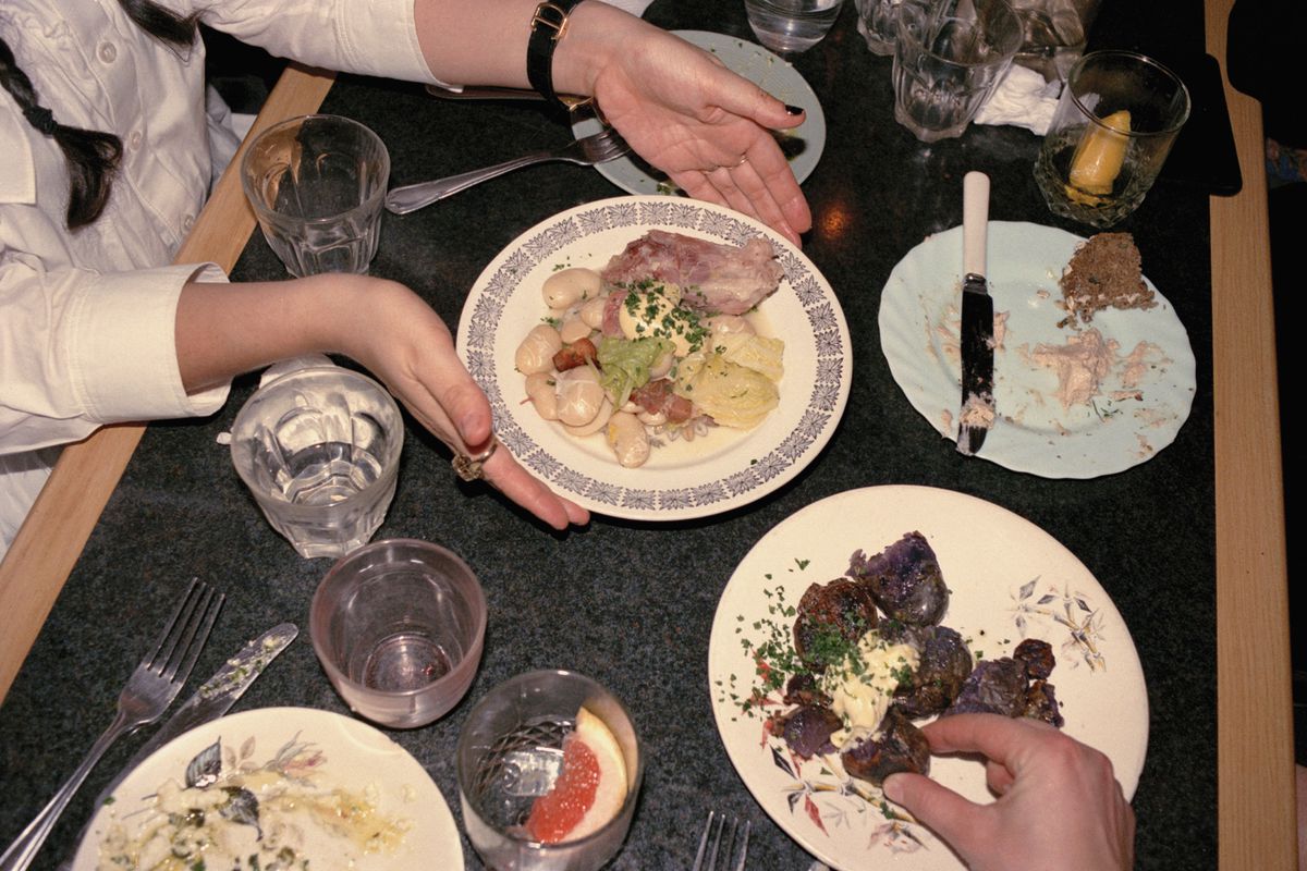 Overhead table shot of someone passing a plate of ham, butter beans, and cabbage at one of ex-River Cafe chef Max Rocha’s first supper clubs, Pacific Social Club in 2016.