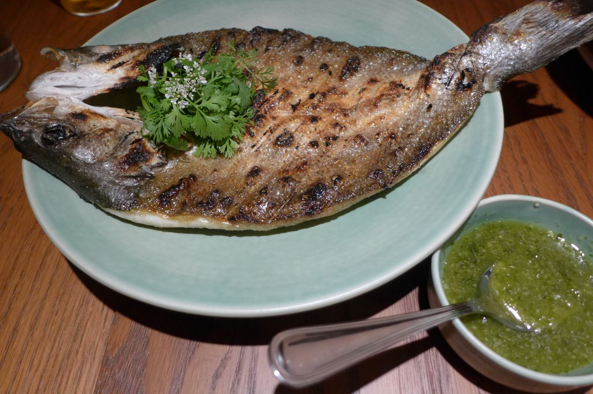 An entire grilled fish with green relish on the side.