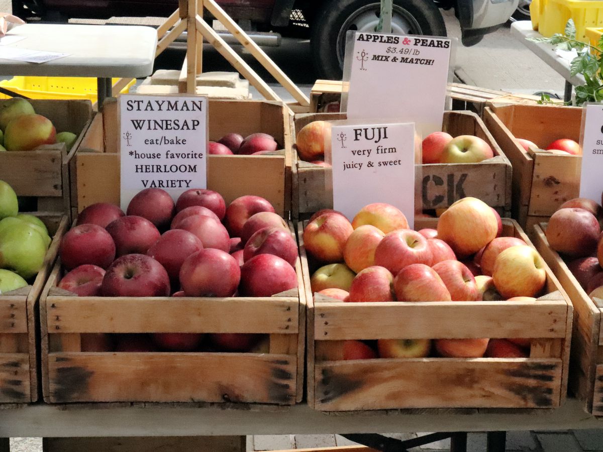 A variety of apples sits in crates at a stand at the FRESHFARM Penn Quarter Market in Washington DC.