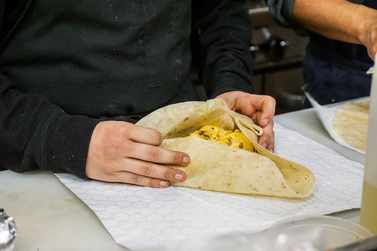 Two hands roll a breakfast burrito inside of a working restaurant.