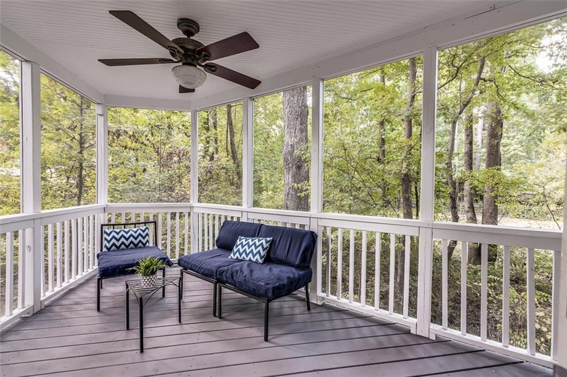 A screened porch near some woods with a ceiling fan overhead.