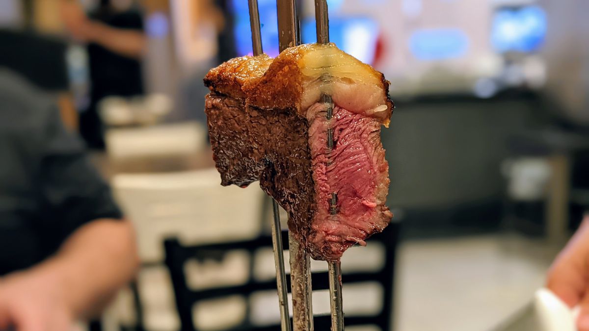 A cut of steak on a skewer with the fat cap still attached.