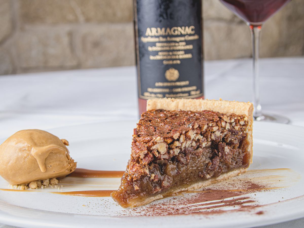 Etoile’s vanilla bourbon pecan pie served with a side of ice cream and caramel drizzle, with a bottle of wine and a glass in the background.