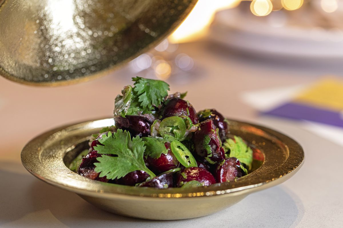 A golden bowl filled with cut red cherries, green cilantro leaves, and slivers of green serrano chilis