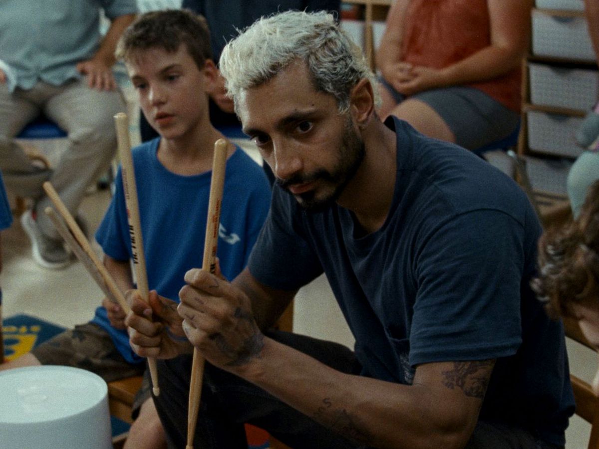 A man sits holding drumsticks to show a group of children.