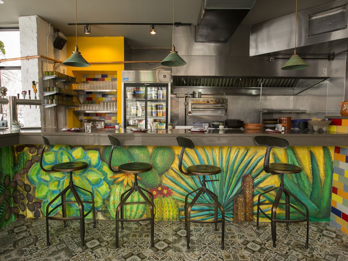 A chef’s counter in front of an open kitchen painted with colorful leaves
