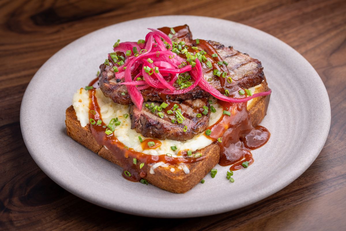 Slices of grilled red meat on a single piece of toast with lots of sauce and pickled red onions.