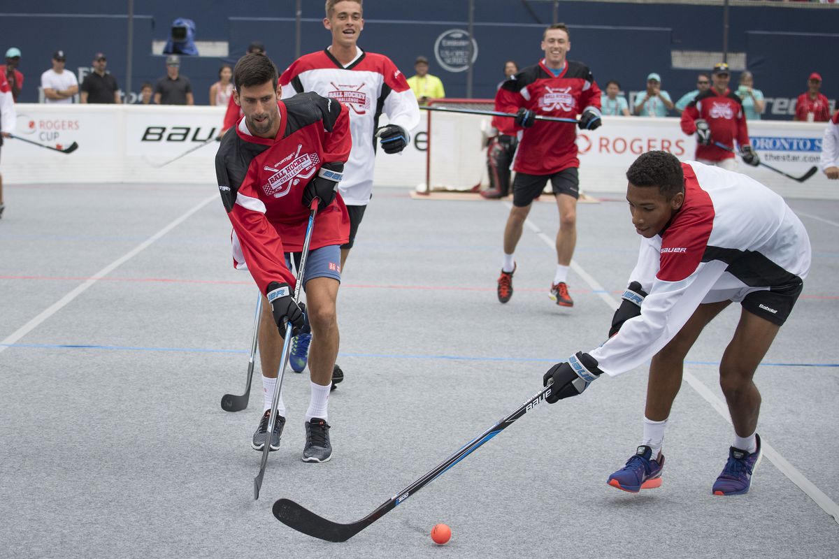 Jul 24, 2016; Toronto, Ontario; Novak Djokovic of Serbia (L) battles for a ball with Felix Auger Aliassime of Canada (R) during the Rogers Cup Sportsnet Ball Hockey Challenge during qualifying of the Rogers Cup tennis tournament at the Aviva Centre. 
